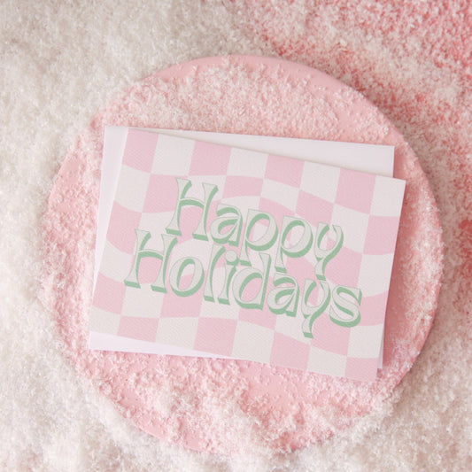 A pink and white checkered card with green and ivory text that reads, "Happy Holidays".