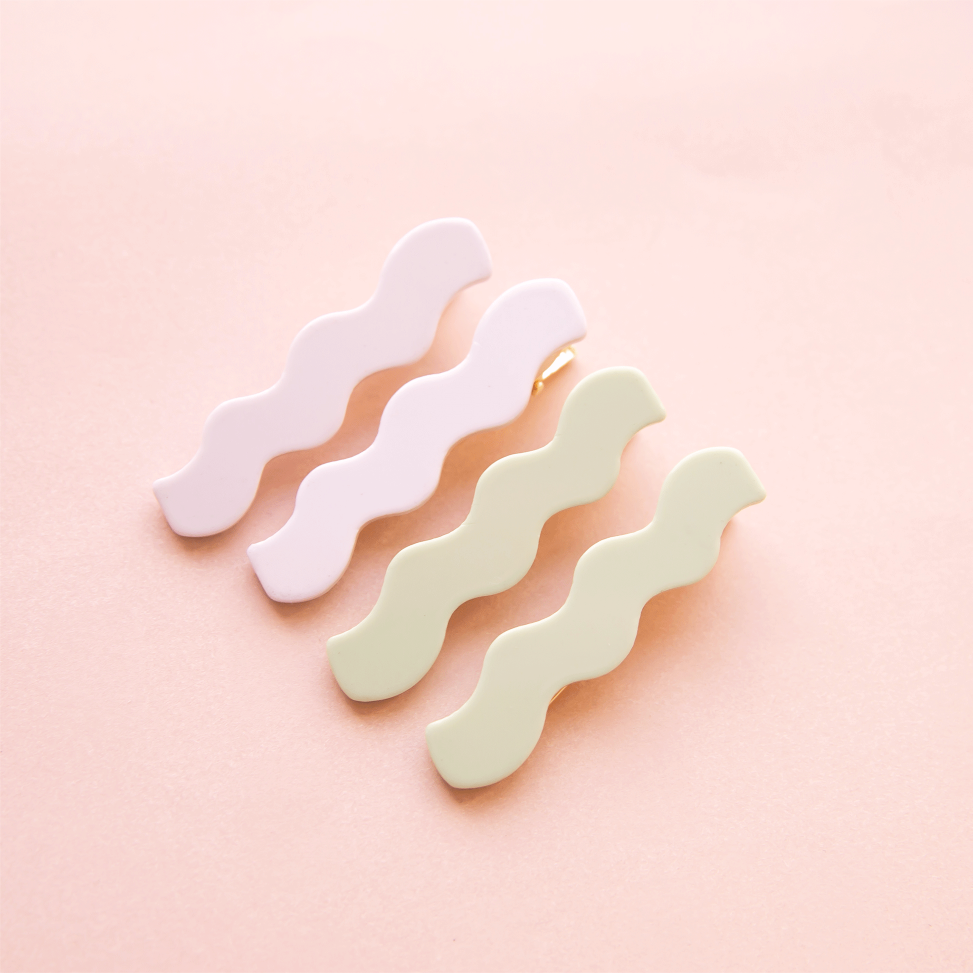 On a pink background is two sets of wavy shaped hair clips in a light green/blue shade and shade of white.