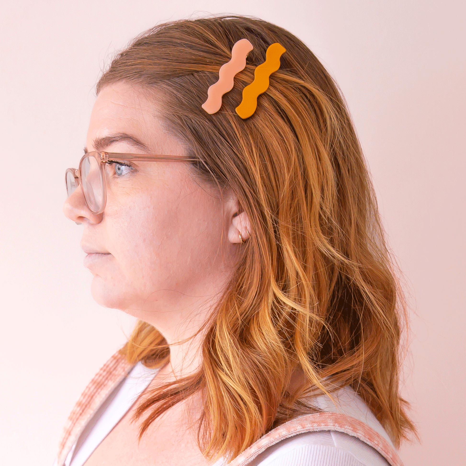 A model wearing the two shades of the wavy hair clips, one orange and one salmon pink.
