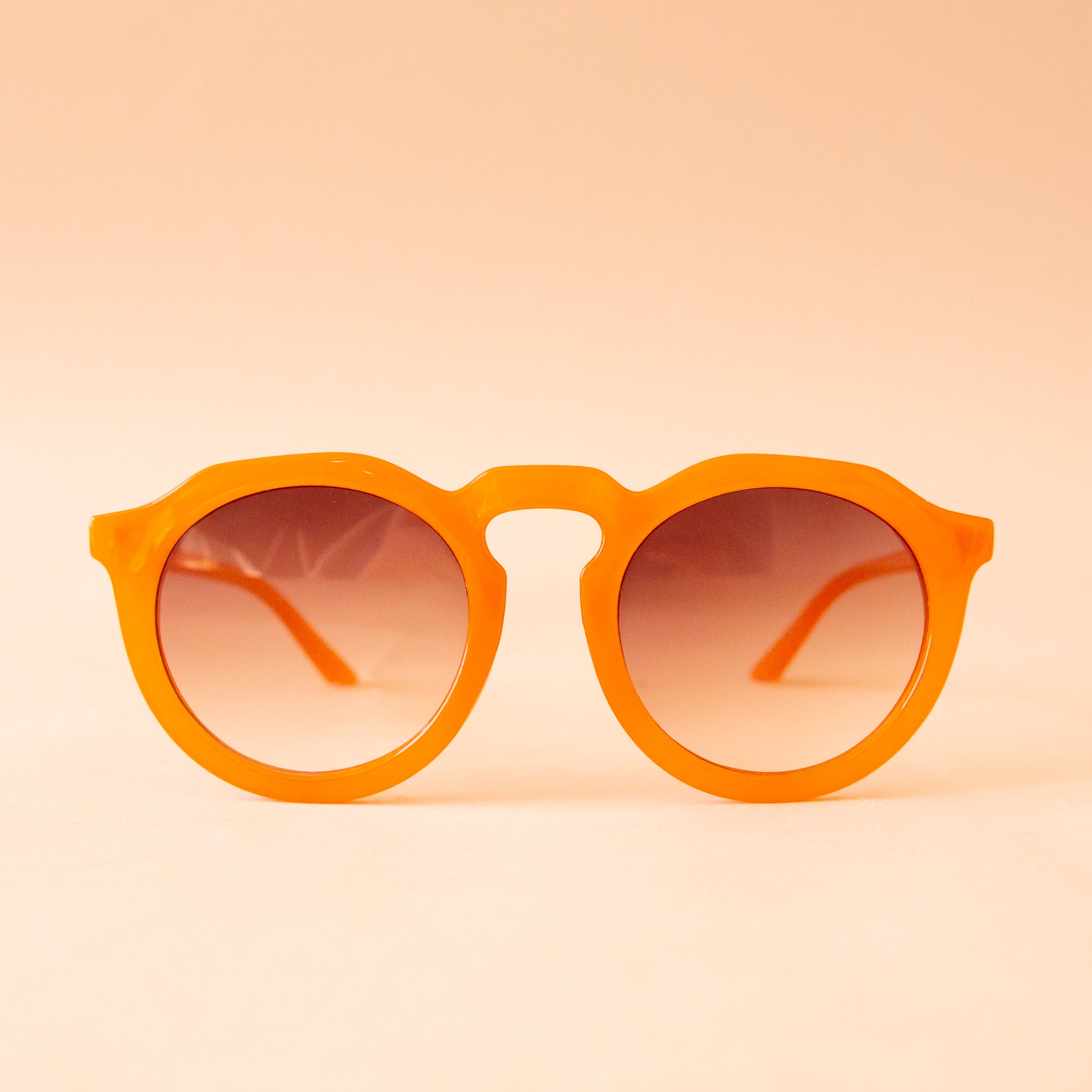 A pair of orange round sunglasses with a brown gradient lens. 