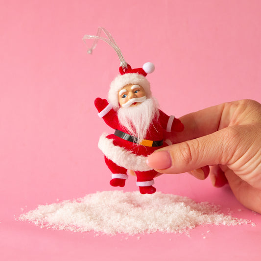 Red flocked dancing Santa ornament against a pink background with fake snow below his feet