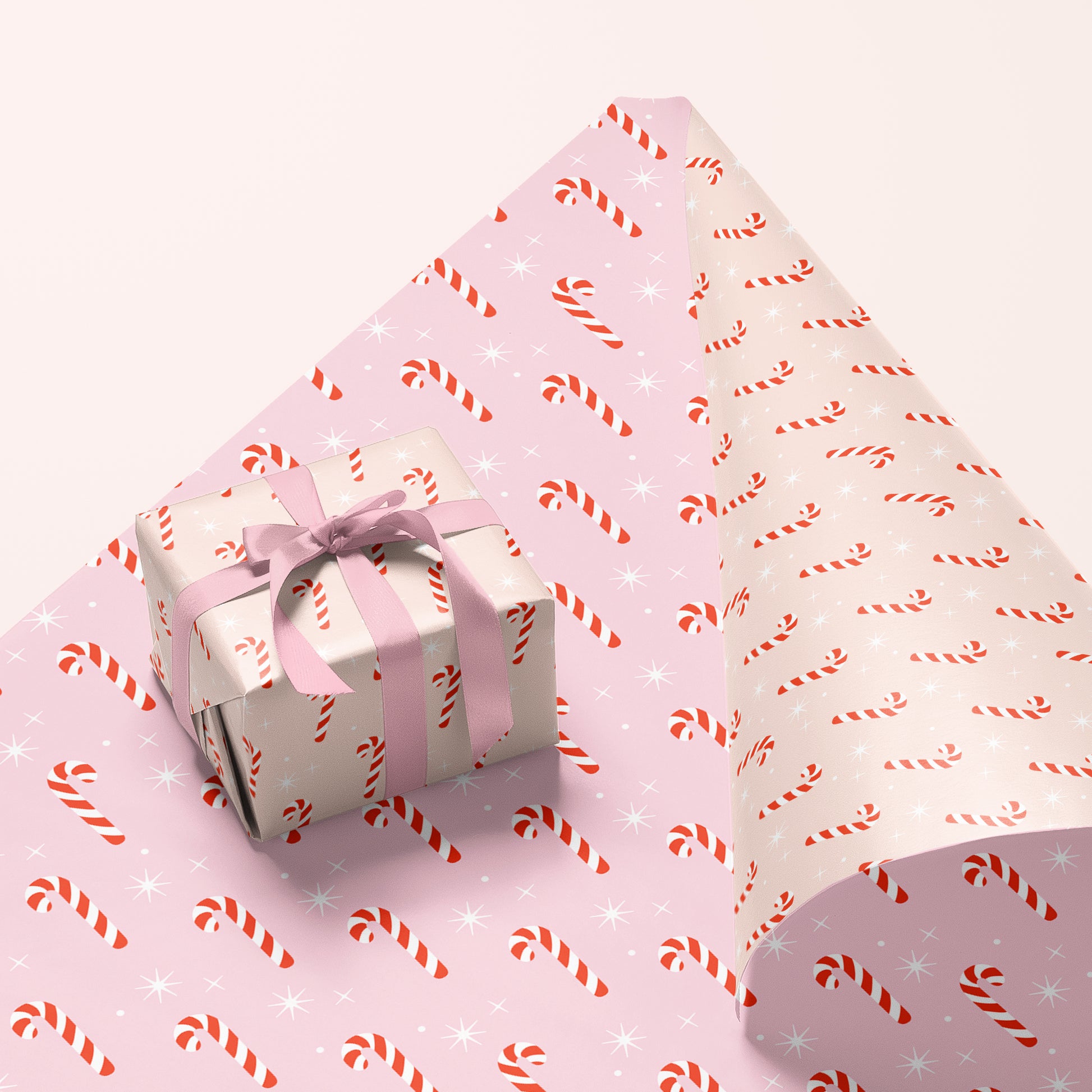 A single sheet of gift wrap with a blush background and a repeating red and white candy cane print. The gift wrap is reversible and the other side features a light purple / lavender background with an all over red and white candy cane design but the candy canes are slightly smaller than the reverse.