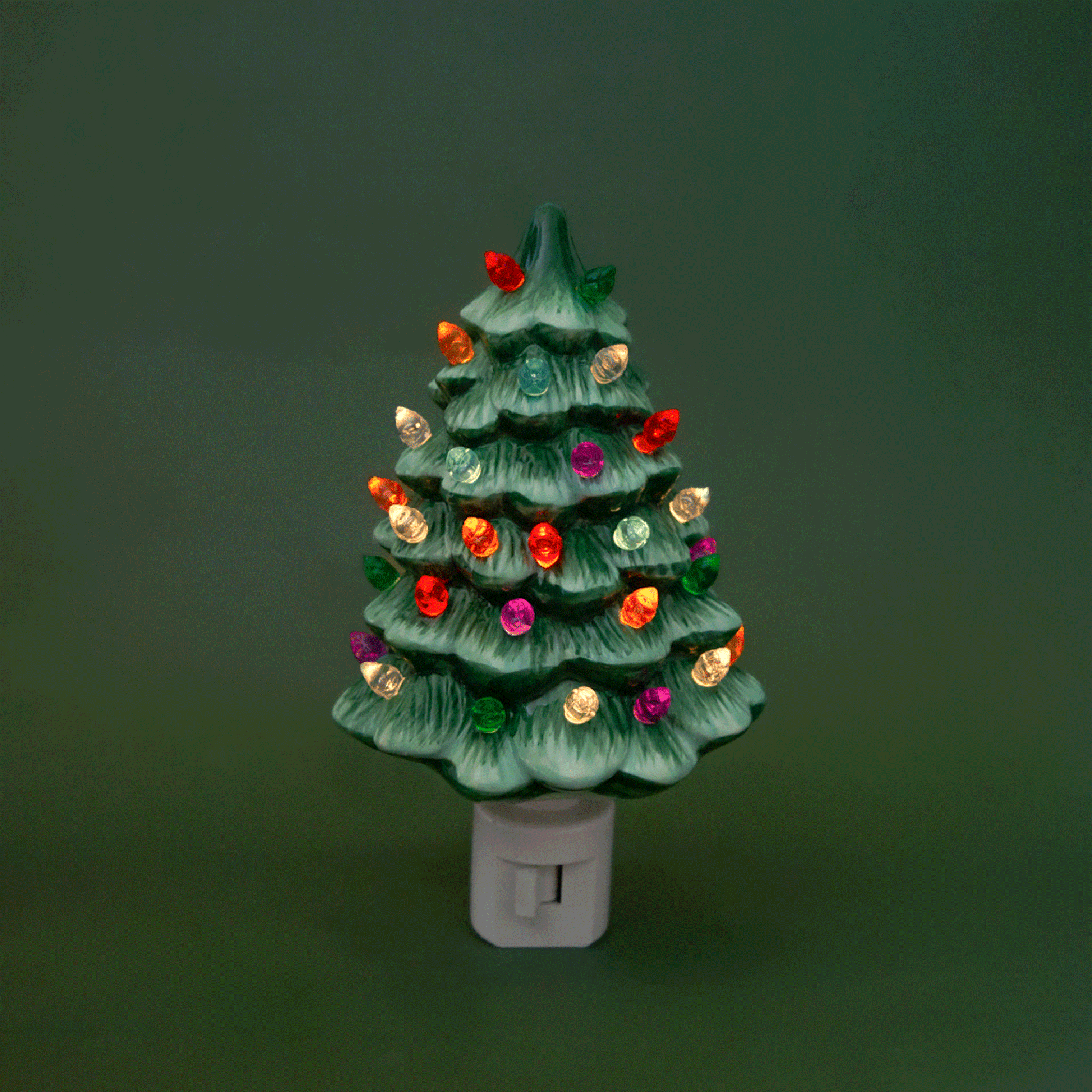 A ceramic Christmas Tree shaped night light sits in middle of the page with bright colorful lights.  It has a white plug at the bottom.  The tree is a green color.