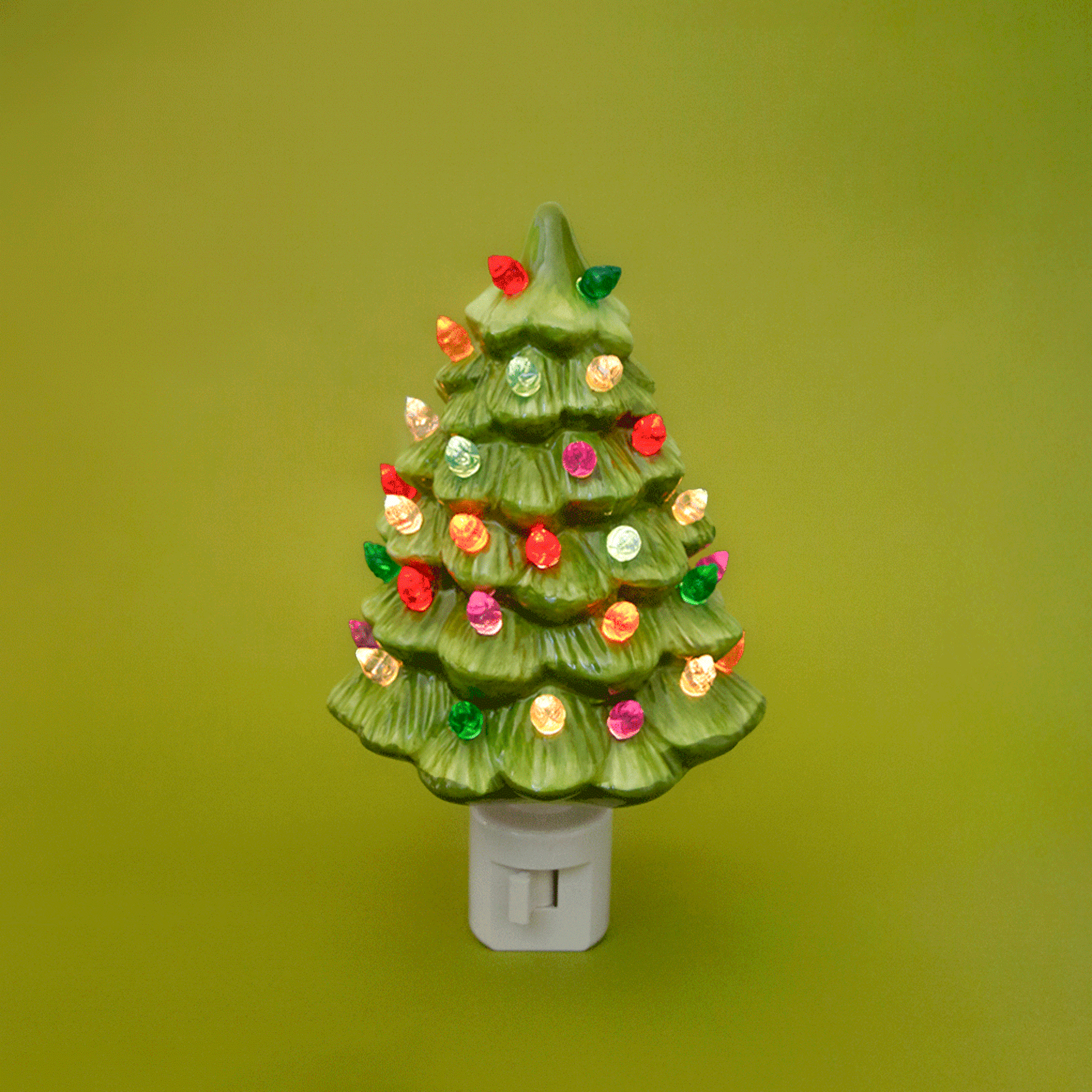 A ceramic Christmas Tree shaped night light sits in middle of the page with bright colorful lights.  It has a white plug at the bottom.  The tree is a lime green color.
