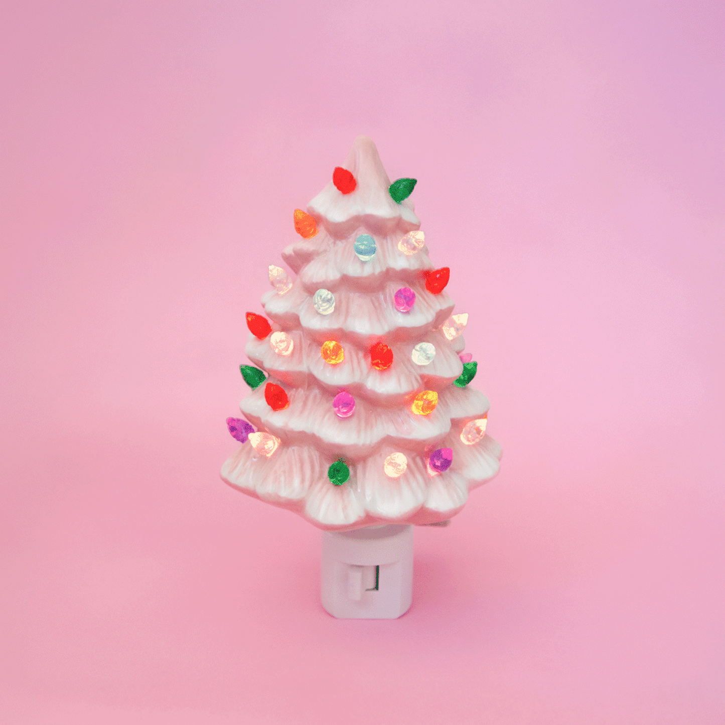 A ceramic christmas tree shaped night light.  The night light has multi colored lights all over it and the ceramic is pink.