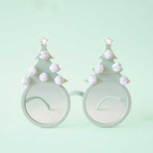 On a mint background is a pair of mint holiday glasses with tree shapes and six white pom poms and a star on top.