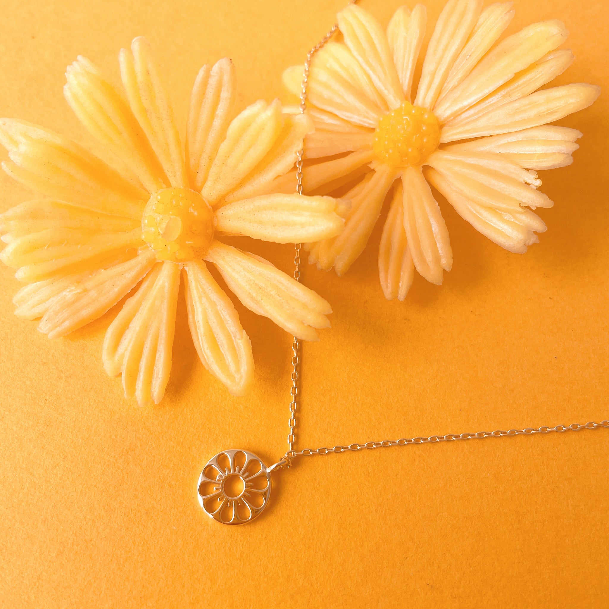 a gold daisy necklace lays on a yellow-orange ground with yellow flowers