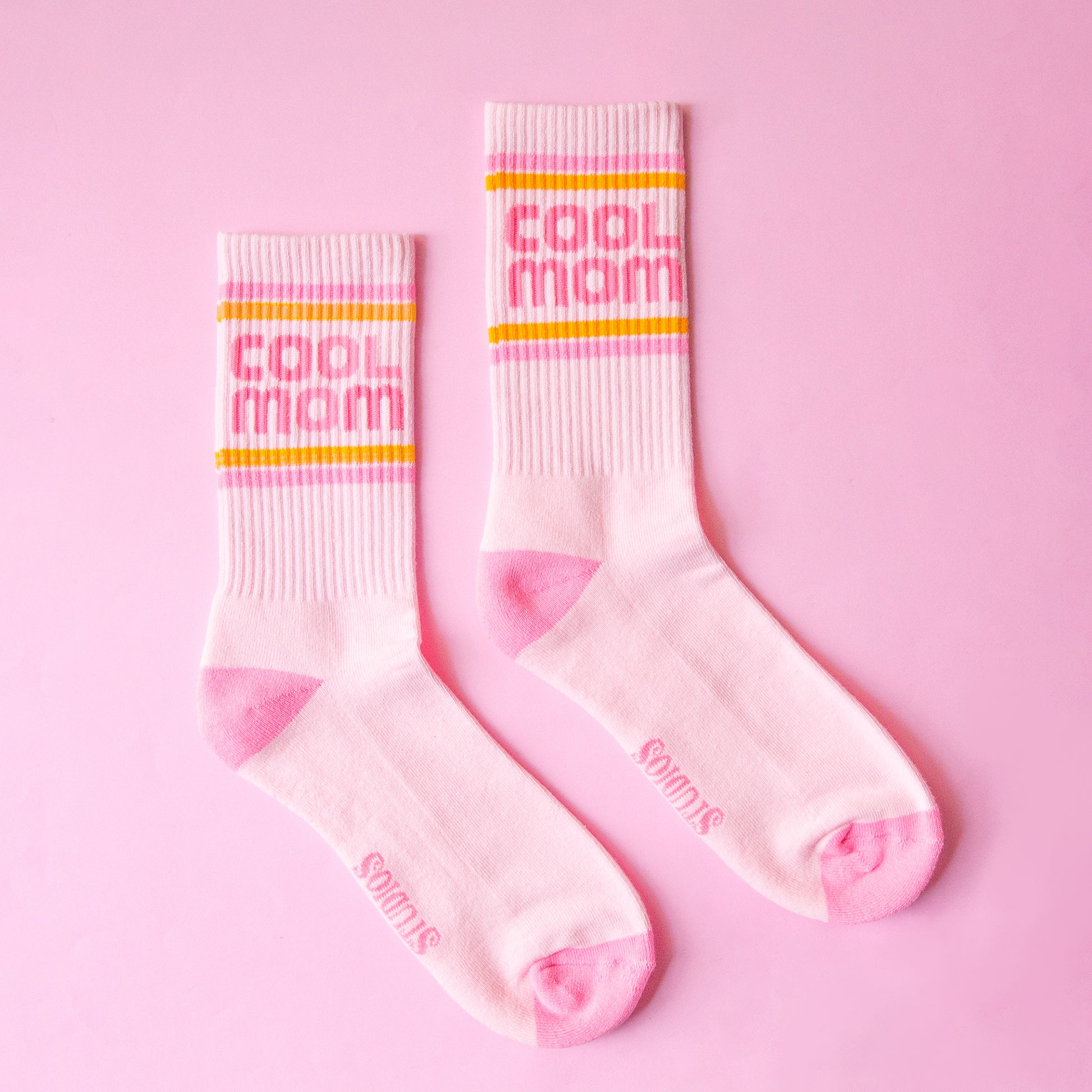 A pair of crew socks with pink and orange stripes and pink text that reads, "cool mom". 