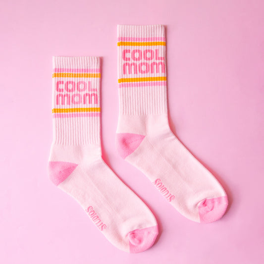 A pair of crew socks with pink and orange stripes and pink text that reads, "cool mom". 