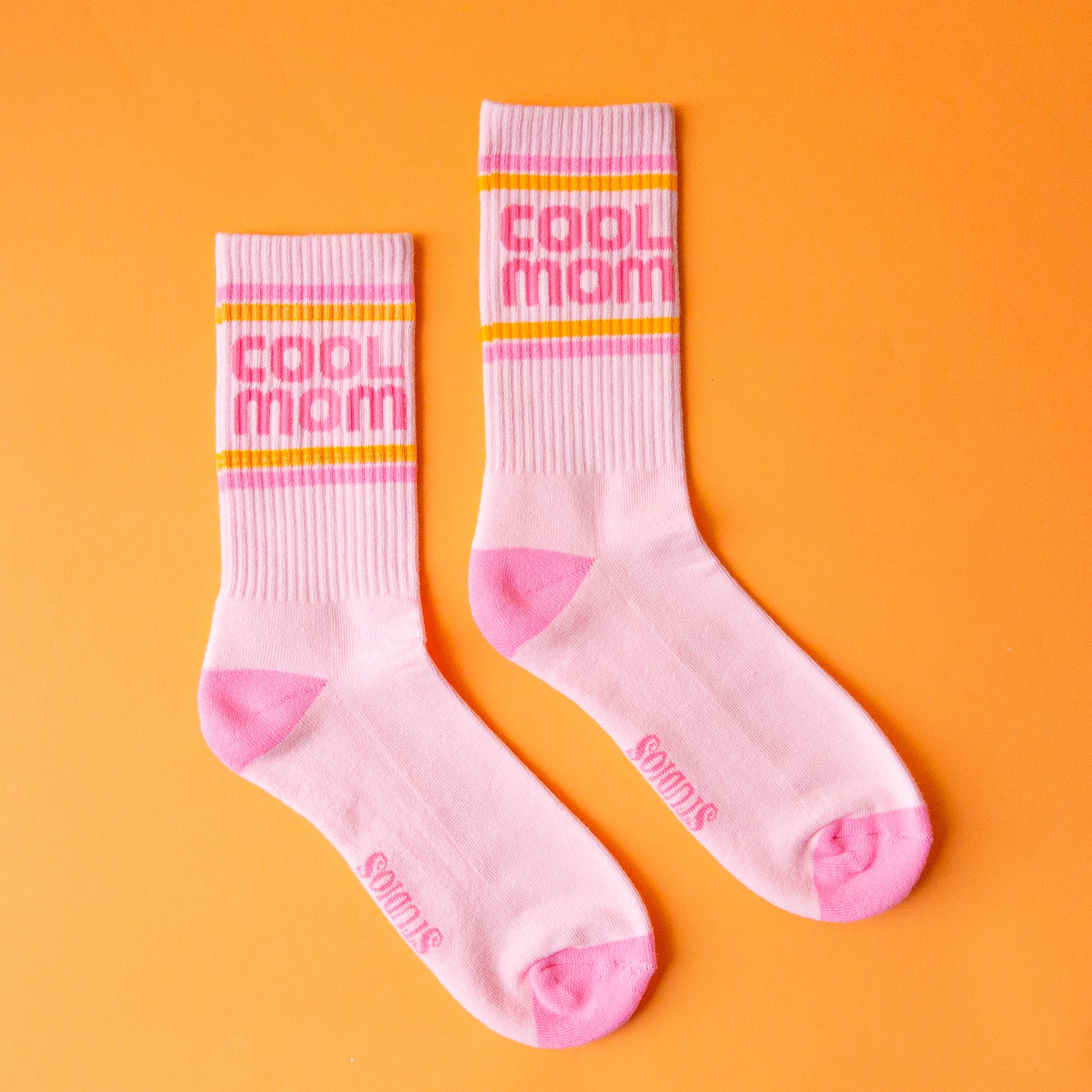 A pair of crew socks with pink and orange stripes and pink text that reads, "cool mom". 