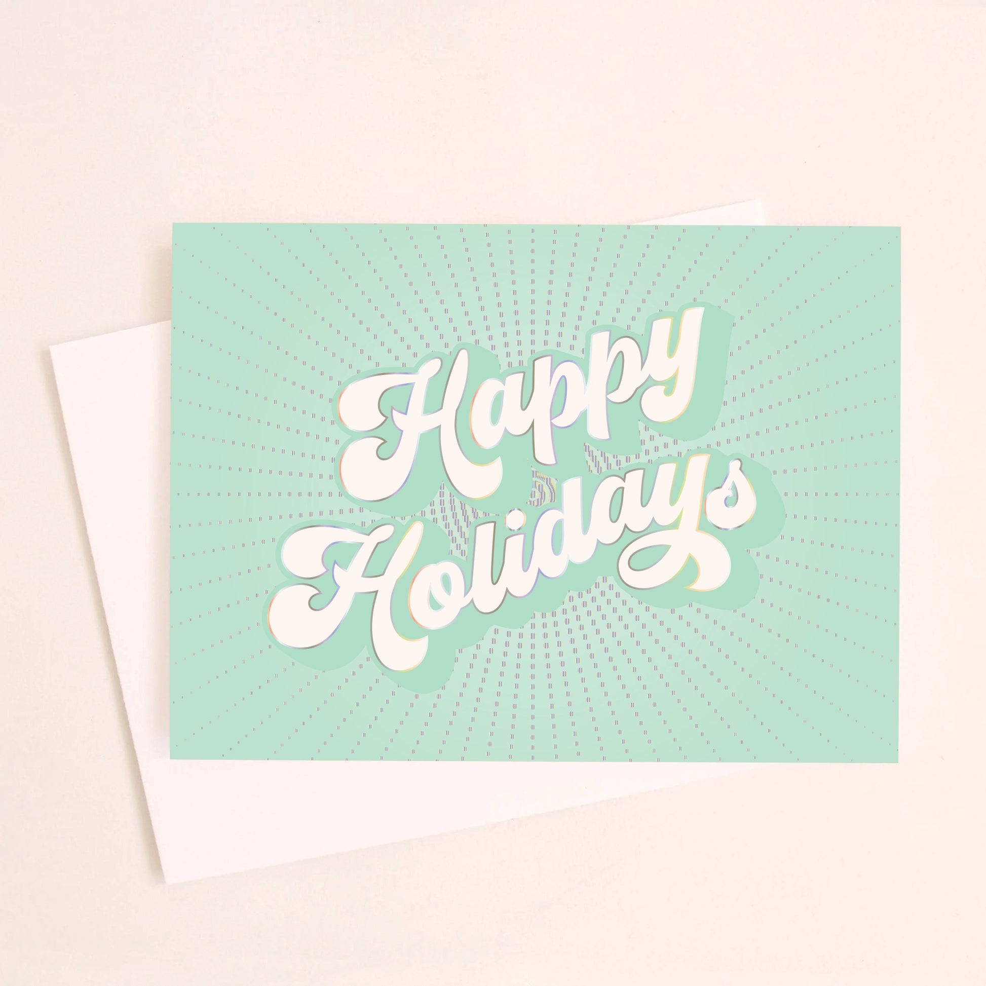 On an ivory background is a teal holiday greeting card with white text that reads, "Happy Holidays" along with a coordinating white envelope. 