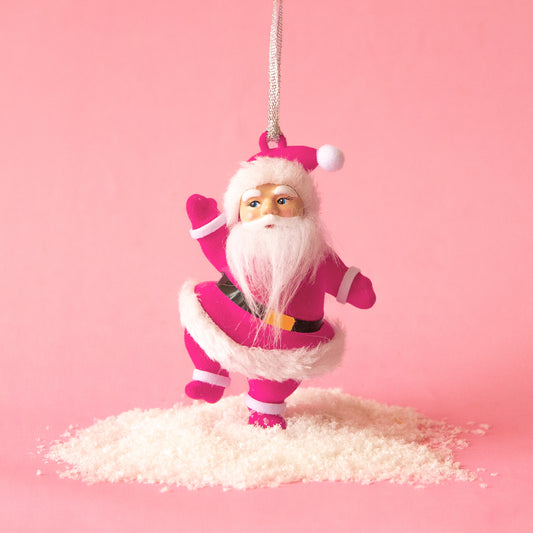 Pink flocked dancing Santa ornament against a pink background with fake snow below his feet