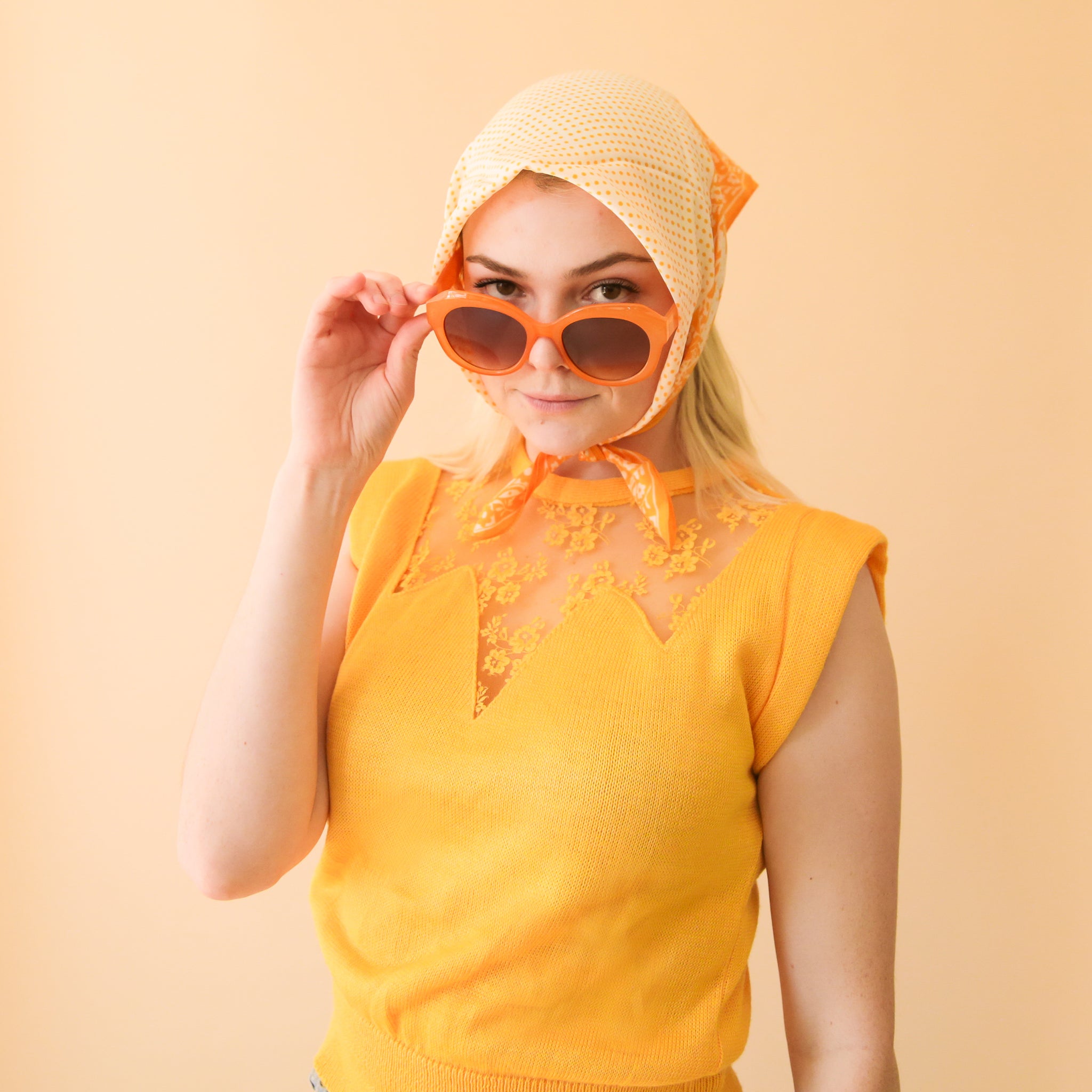 a woman poses with orange retro styled sunglasses
