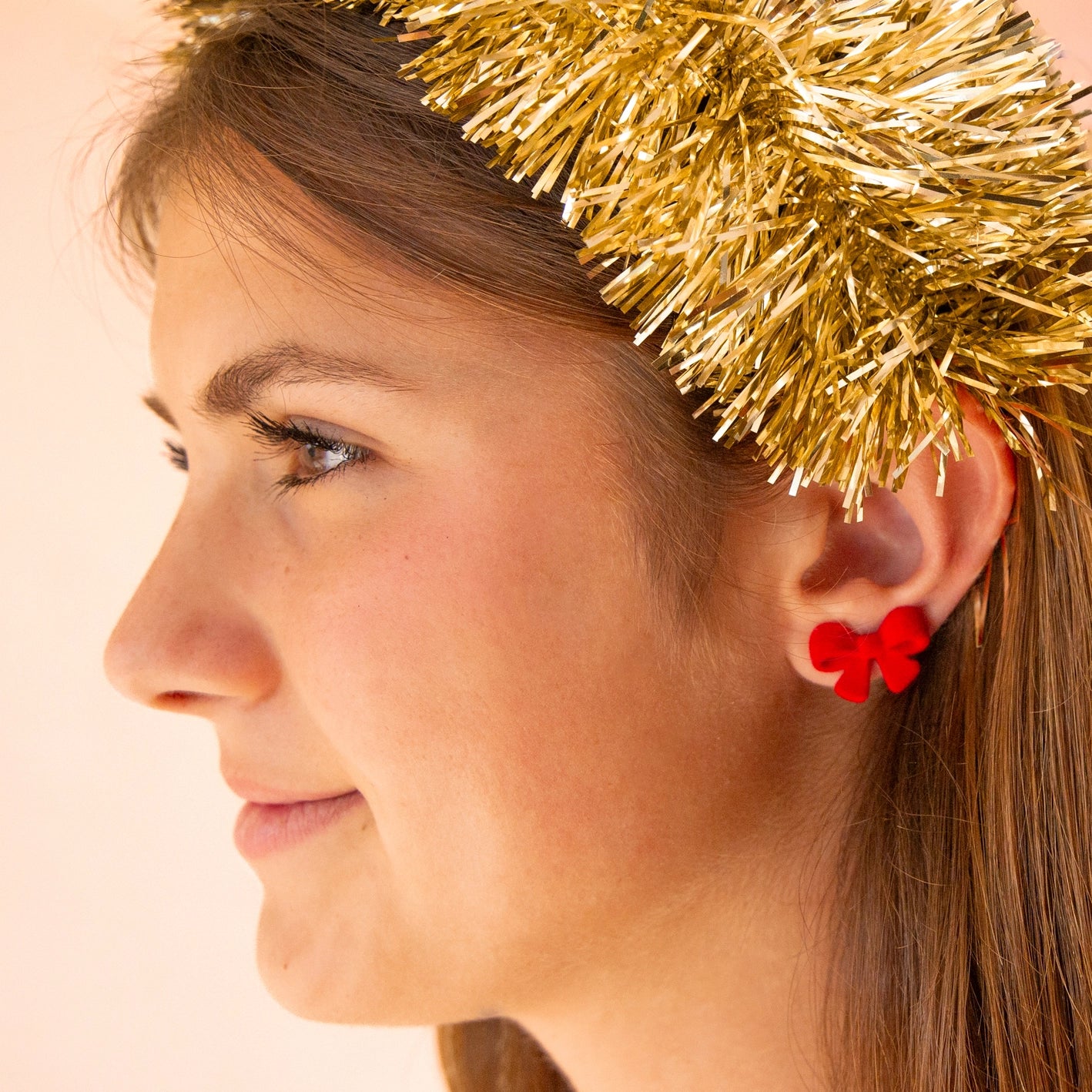 Model wearing flocked red bow earrings and a gold tinsel headband. 