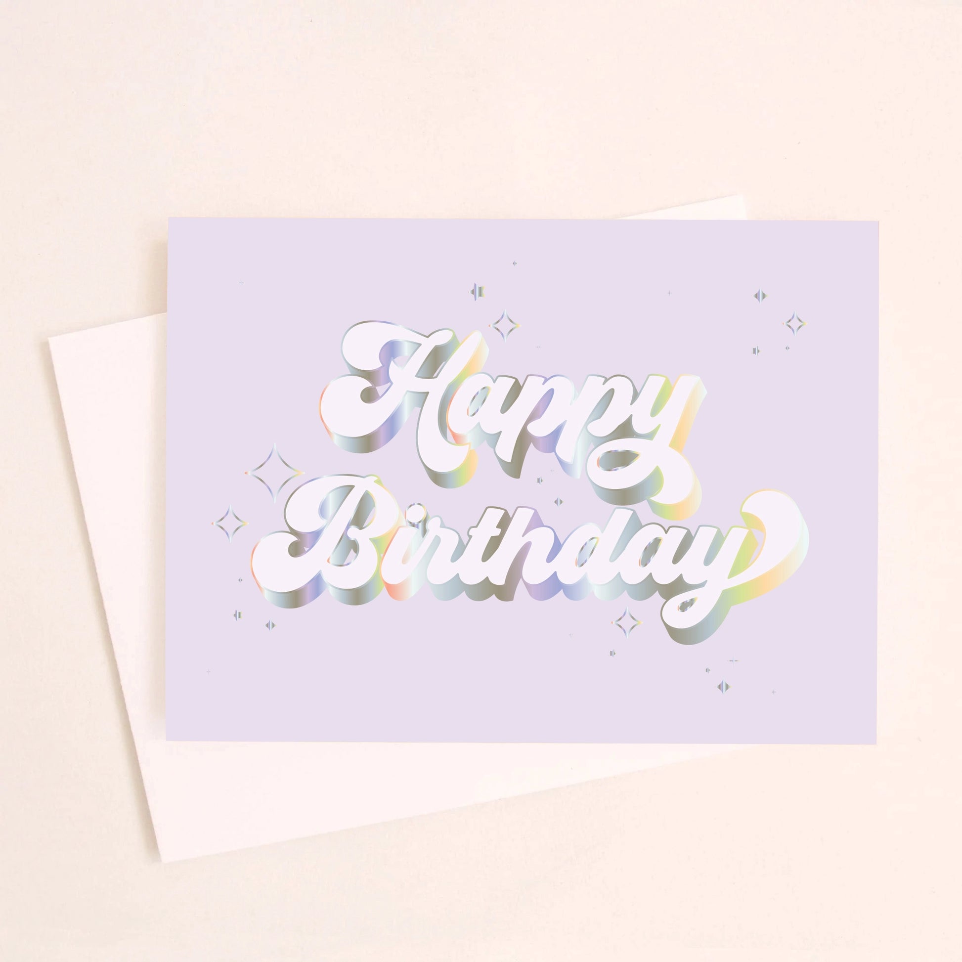 On an ivory background is a light purple/blue greeting card with white / holographic outlined text that reads, "Happy Birthday" along with a white envelope. 