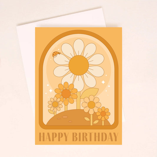 On an ivory background is an orange greeting card with a darker orange arched border and daisy illustrations inside along with text at the bottom that reads, "Happy Birthday". Also included is a white envelope. 
