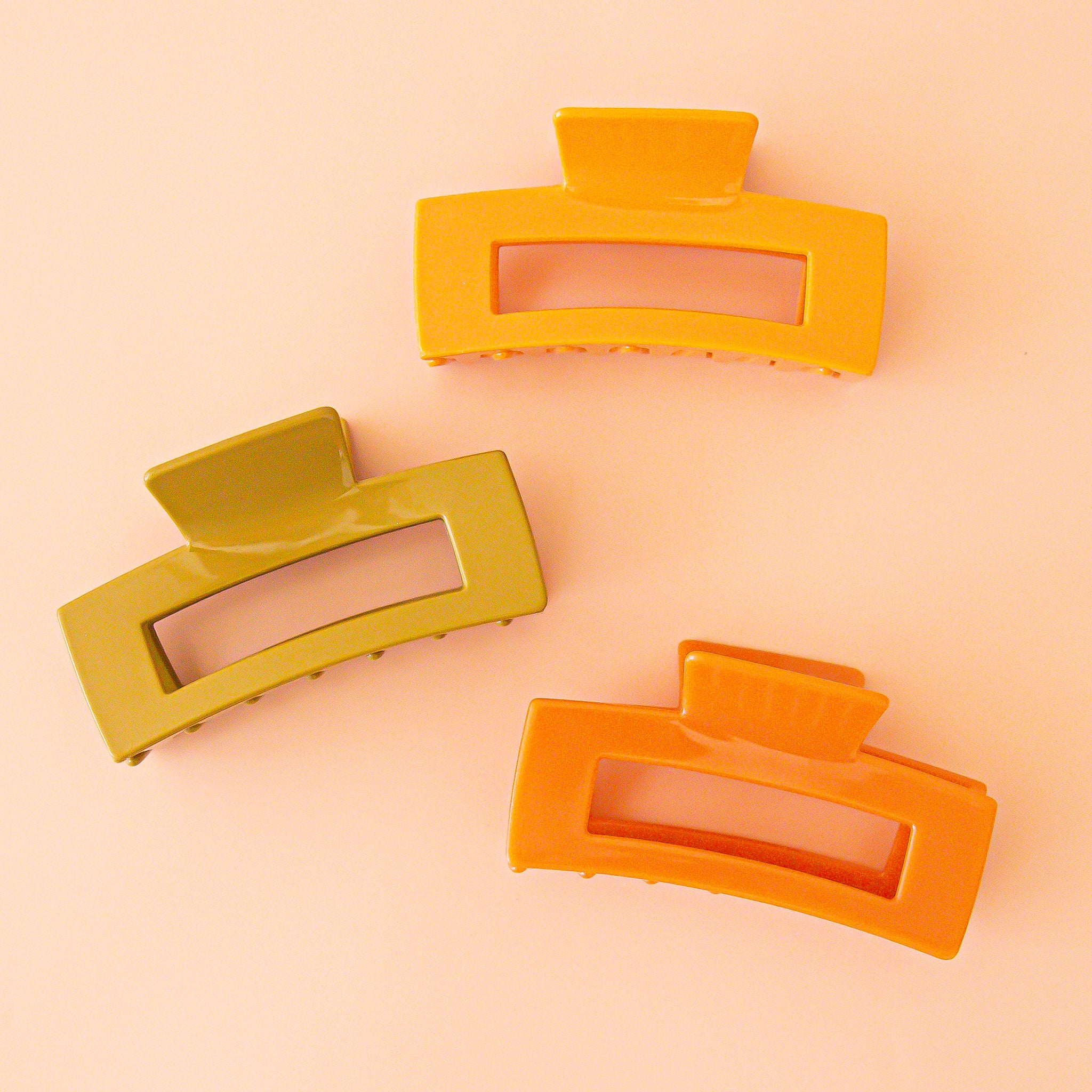 three hair claws in yellow, olive, and orange colors lie flat on peach ground