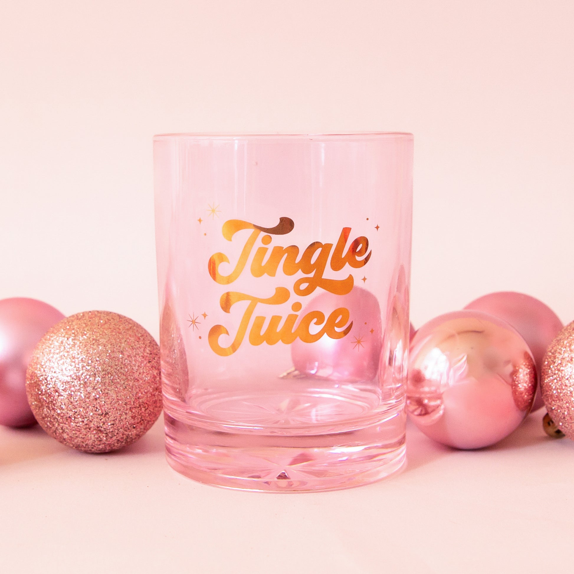 Glass cup with gold lettering is shown against a pink background