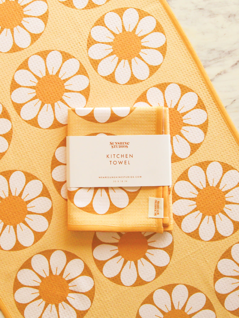 a yellow and orange kitchen towel with retro circle flowers lays flat on a counter with a folder towel on top