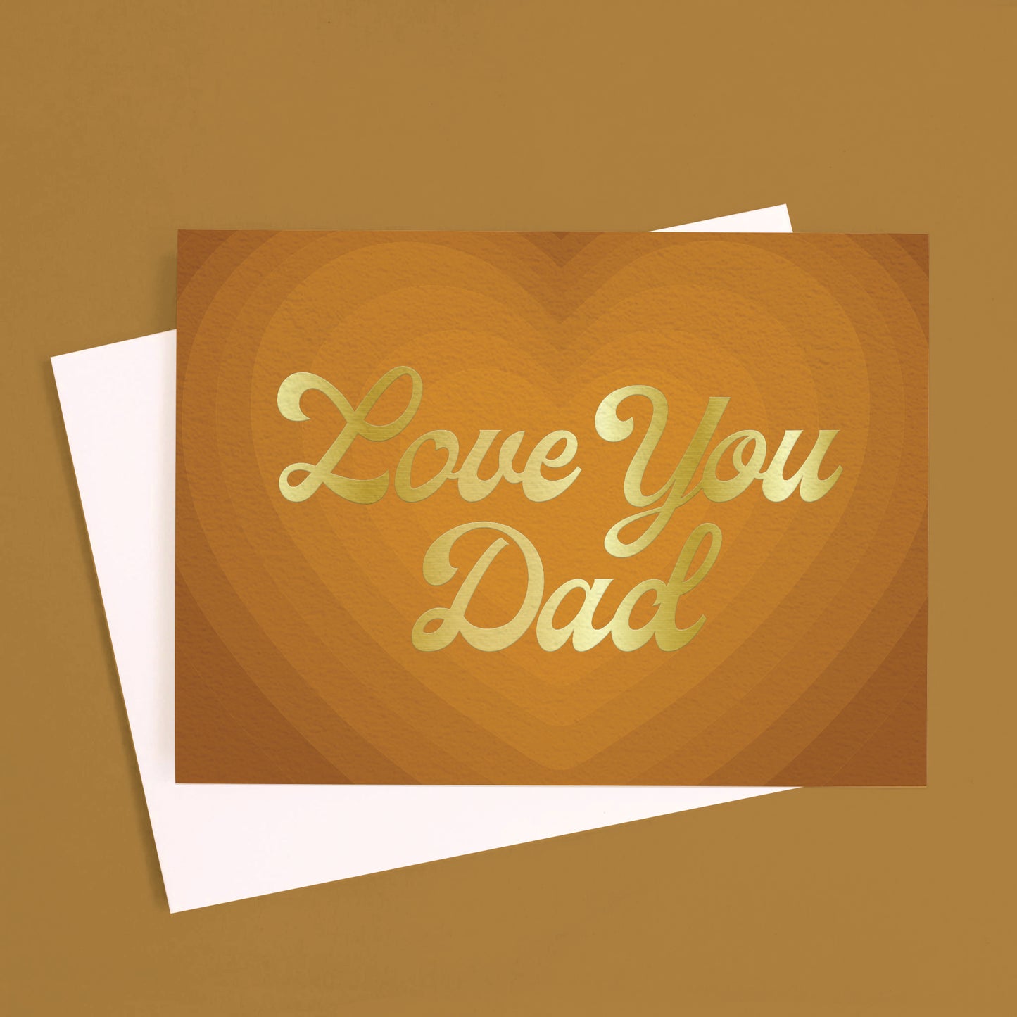 On a light brown background is a brown card with a radiating heart card and gold foiled text that reads, "Love You Dad". 