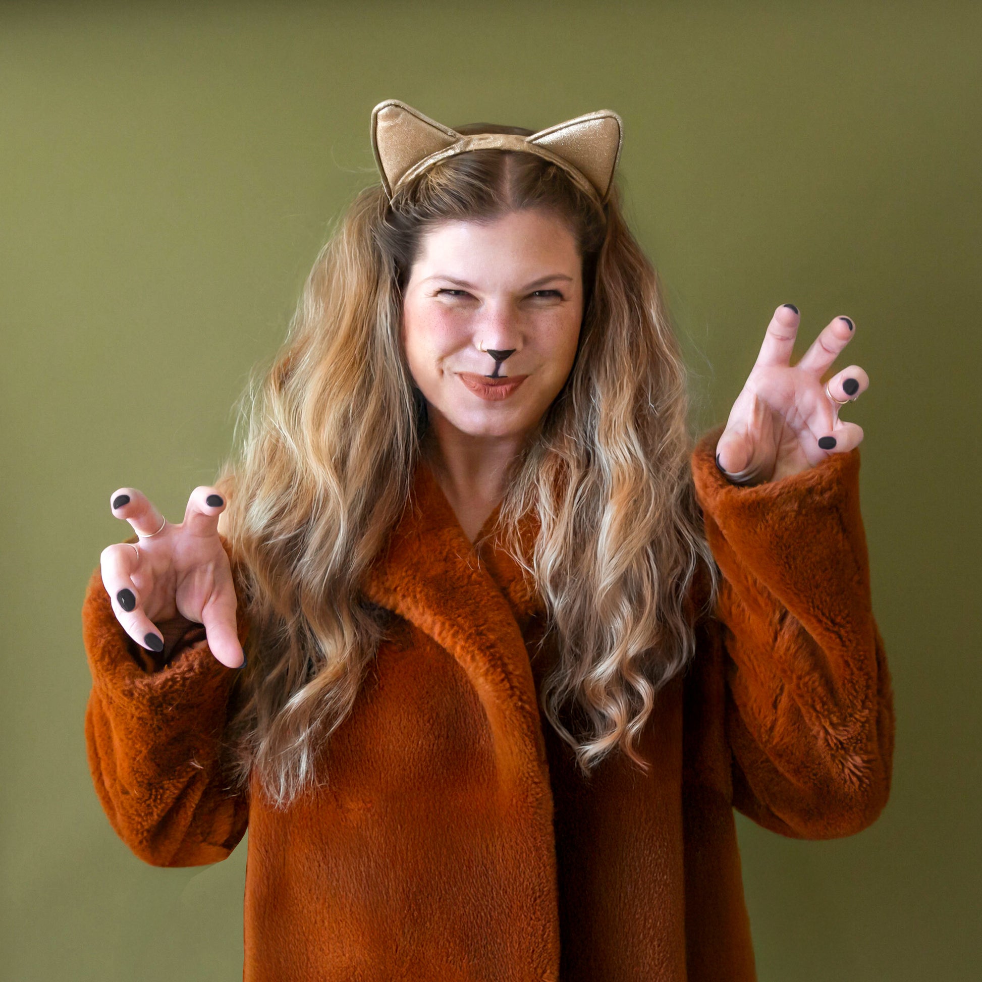 Model in leopard body suit with red hair wears a gold glitter cat ears headband.