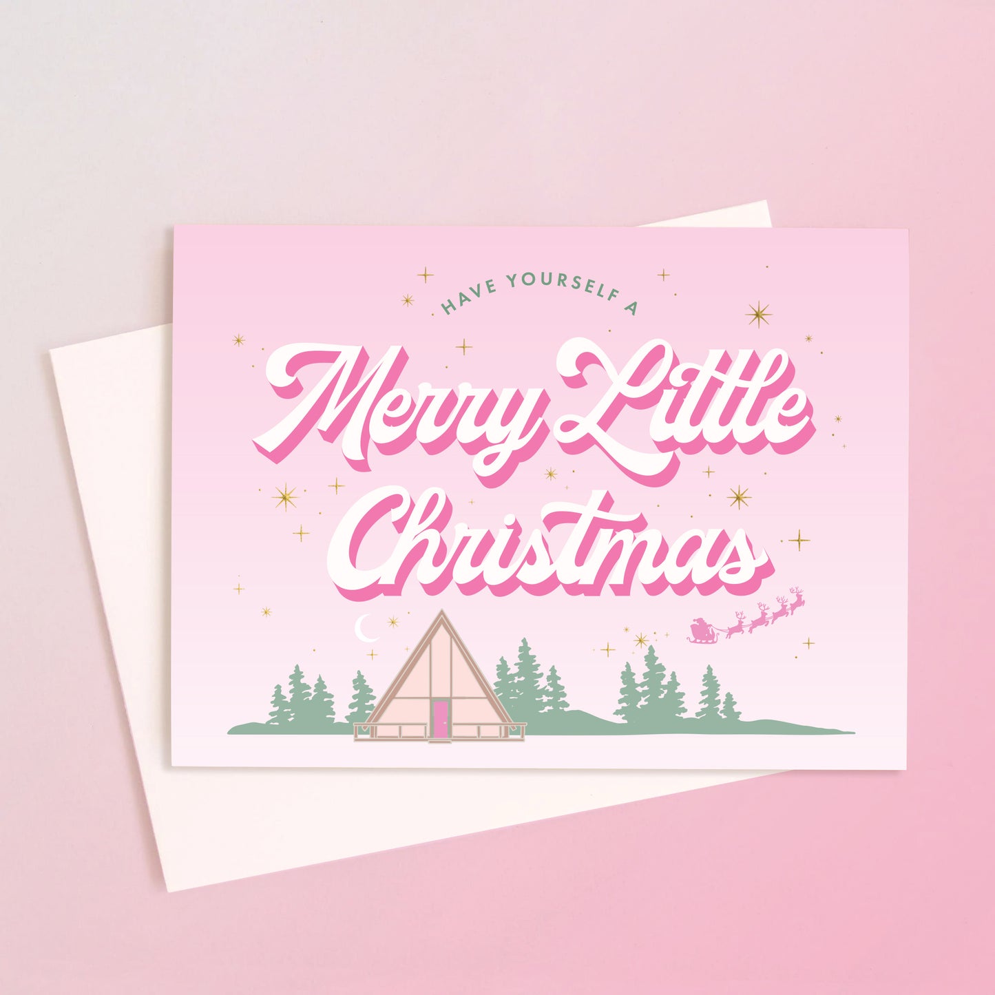 A light pink card with a retro A-frame cabin graphic with text above that reads, 'Have Yourself A Merry Little Christmas'. 