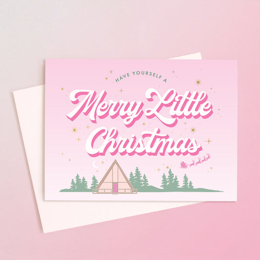 A light pink card with a retro A-frame cabin graphic with text above that reads, 'Have Yourself A Merry Little Christmas'. 
