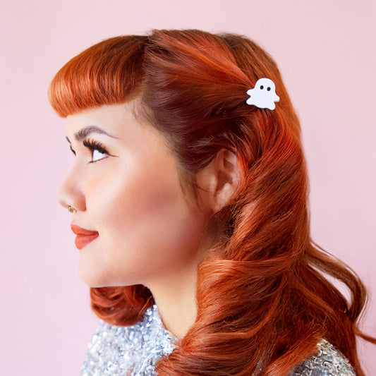A red headed model wears a ghost shaped clip in her hair.  She has soft curls and red lipstick on.