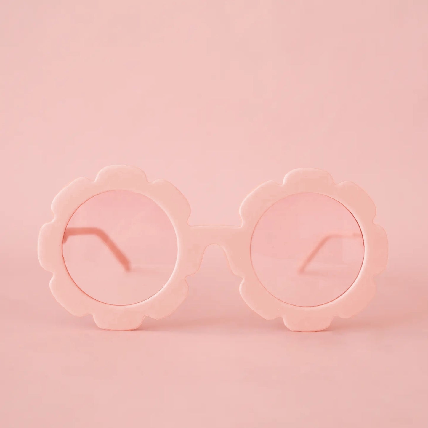 On a pink background is a pink pair of flower shaped sunglasses with a light pink circle lens in the center. 