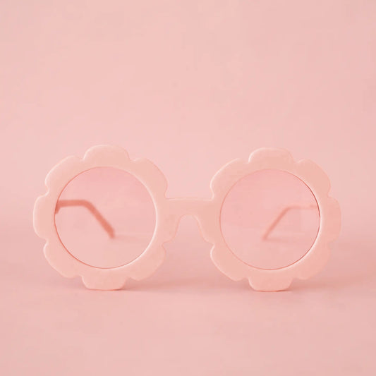 On a pink background is a pink pair of flower shaped sunglasses with a light pink circle lens in the center. 