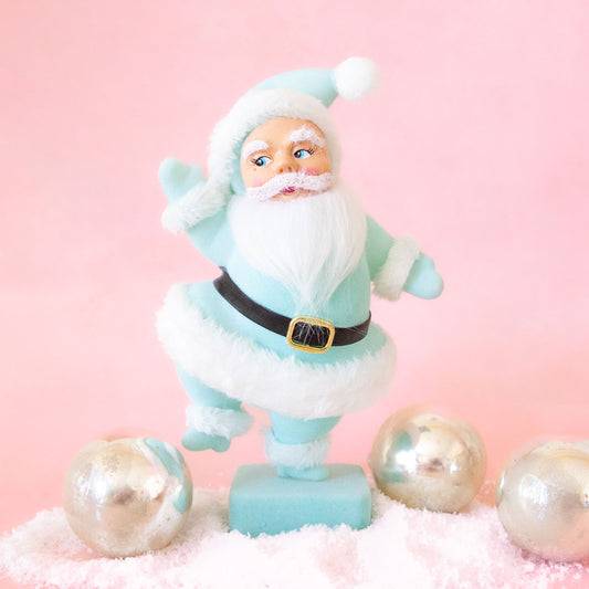 On a pink background is a Santa figurine wearing a mint colored suit with the fluffy details. 