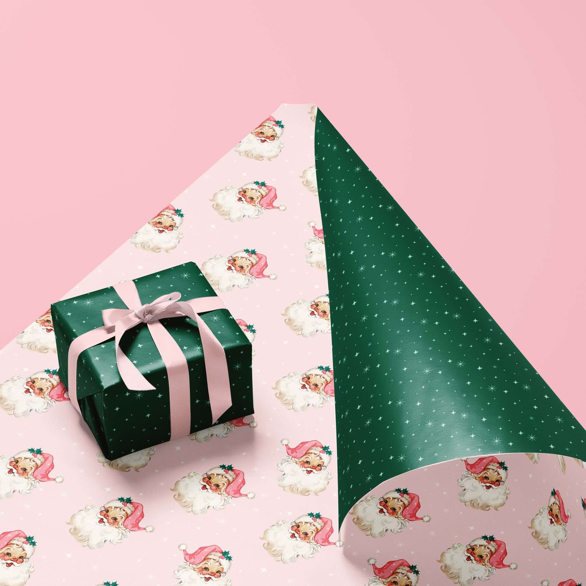 Holiday wrapping paper. One side is light pink with retro inspired Santa Clause faces and the other side is emerald green with white stars. 
