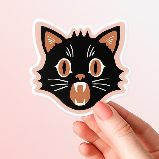 Hand holding a sticker of a black cat face with orange details. 