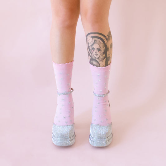 A figure wearing baby pink socks with silver stars and tall shiny silver platform shoes.