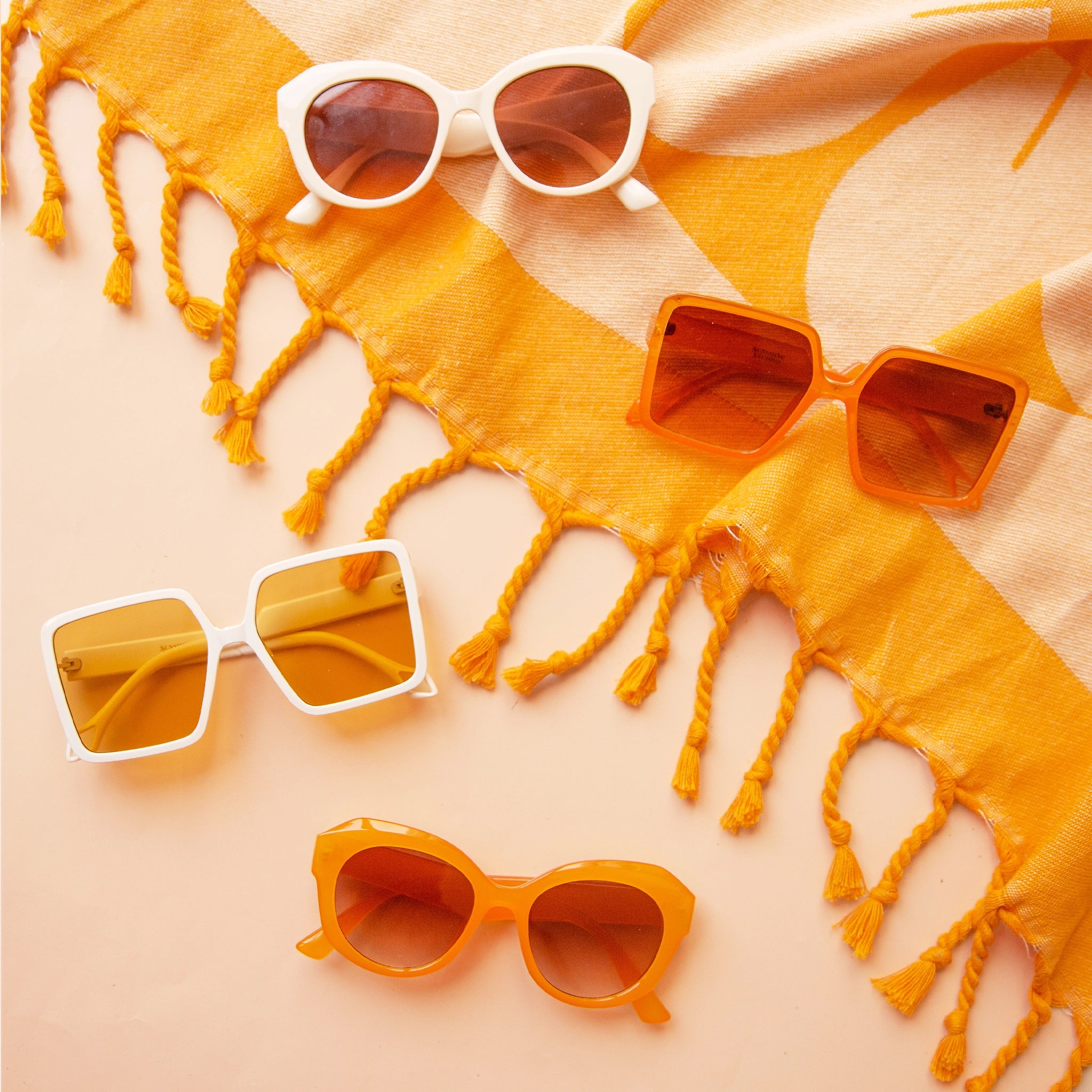 four pairs of sunglasses in various shapes and colors lie flat on a yellow beach towel