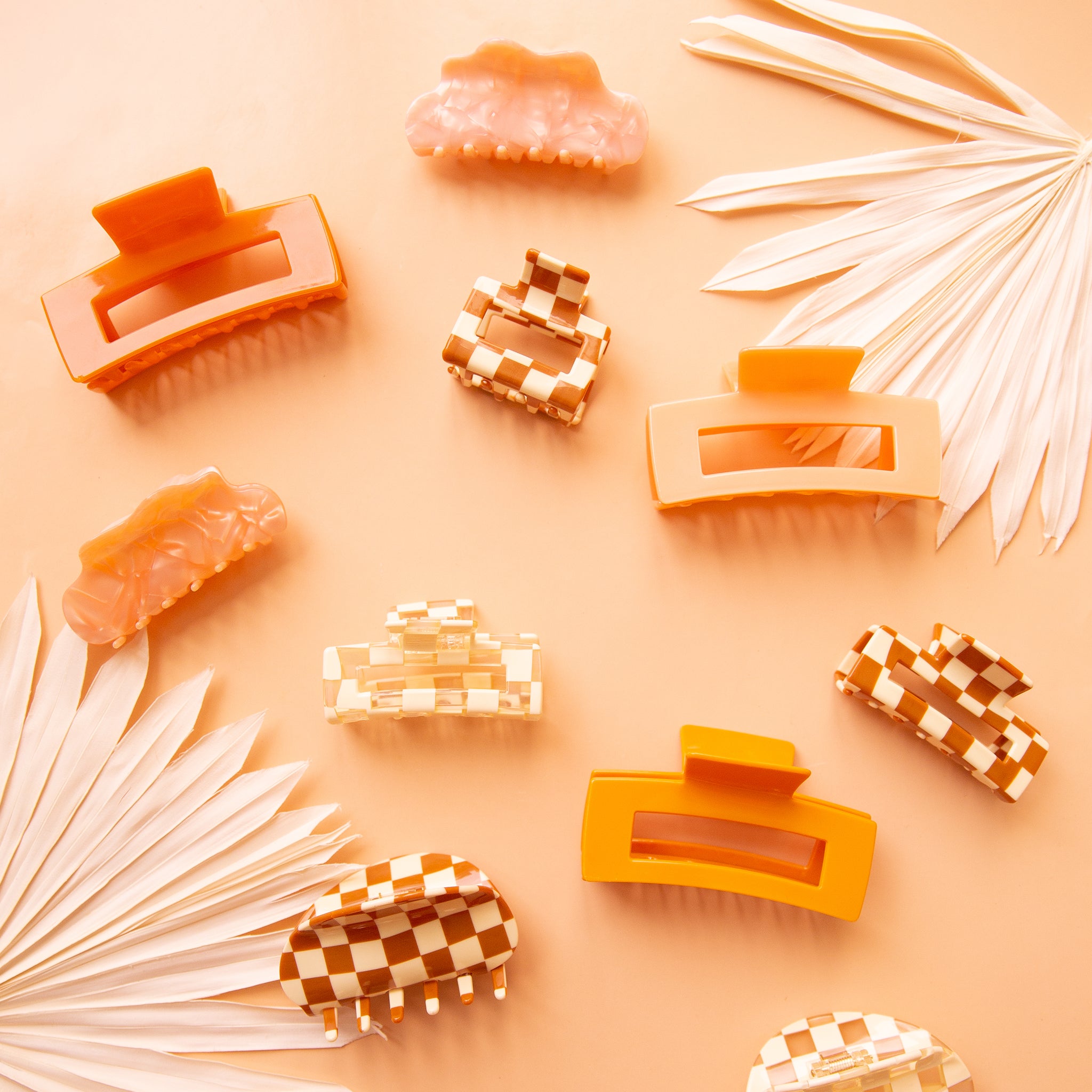 hair claws in various shapes and colors lie on a peach ground with white dried palms