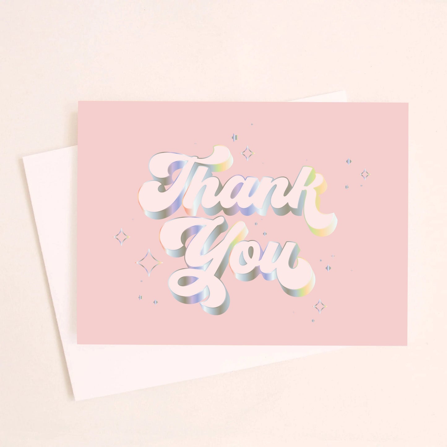 On an ivory background is a light pink card that reads, "Thank You" with in white text with holographic outlining. 