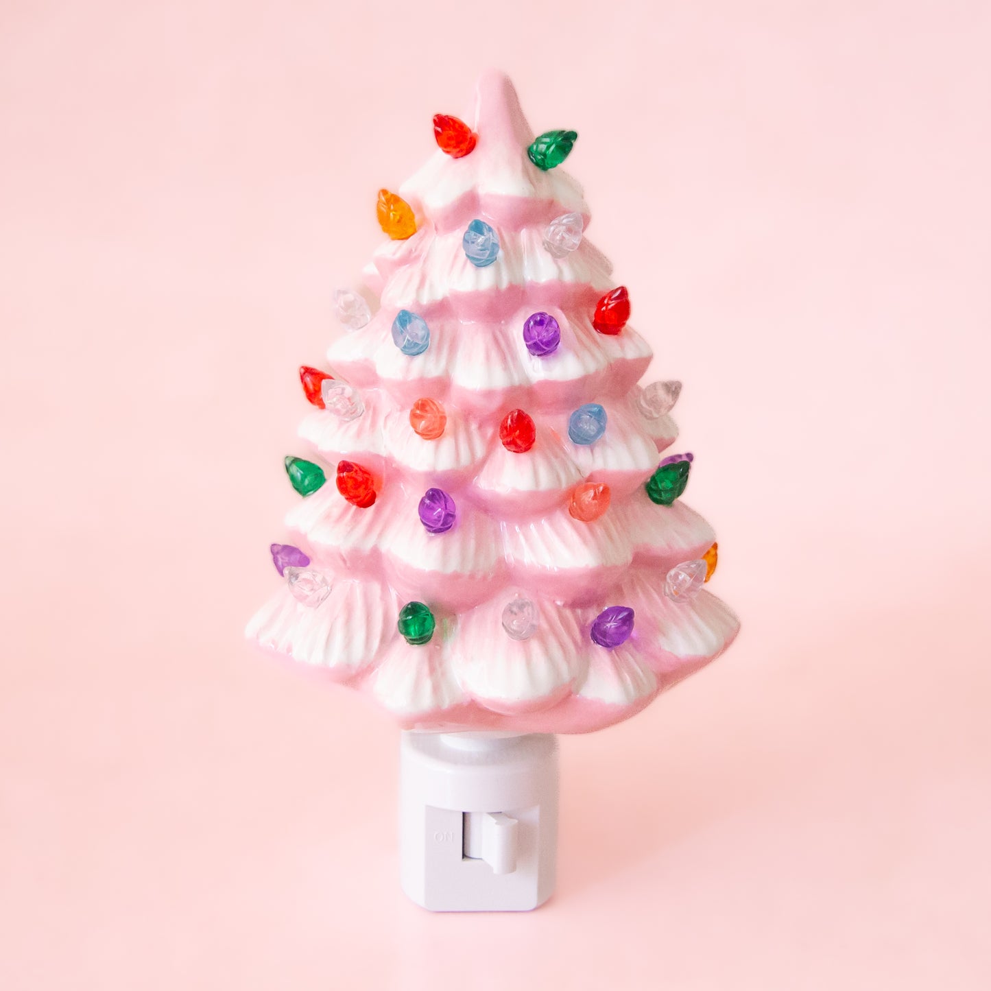 A ceramic christmas tree shaped night light.  The night light has multi colored lights all over it and the ceramic is pink.