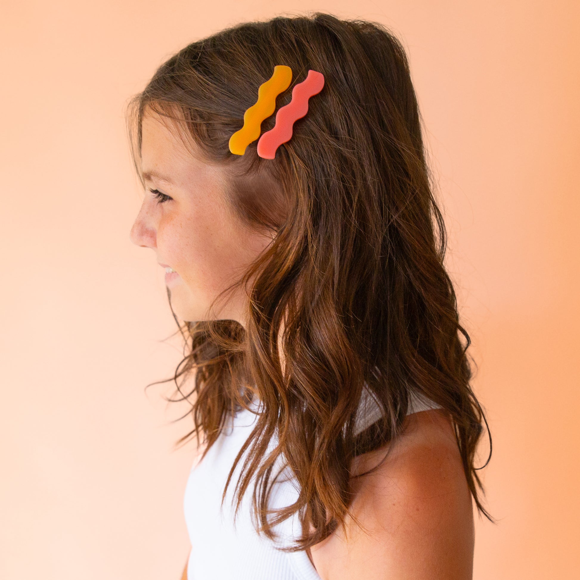 Two wavy hair clips in a tangerine shade and a pink color. 