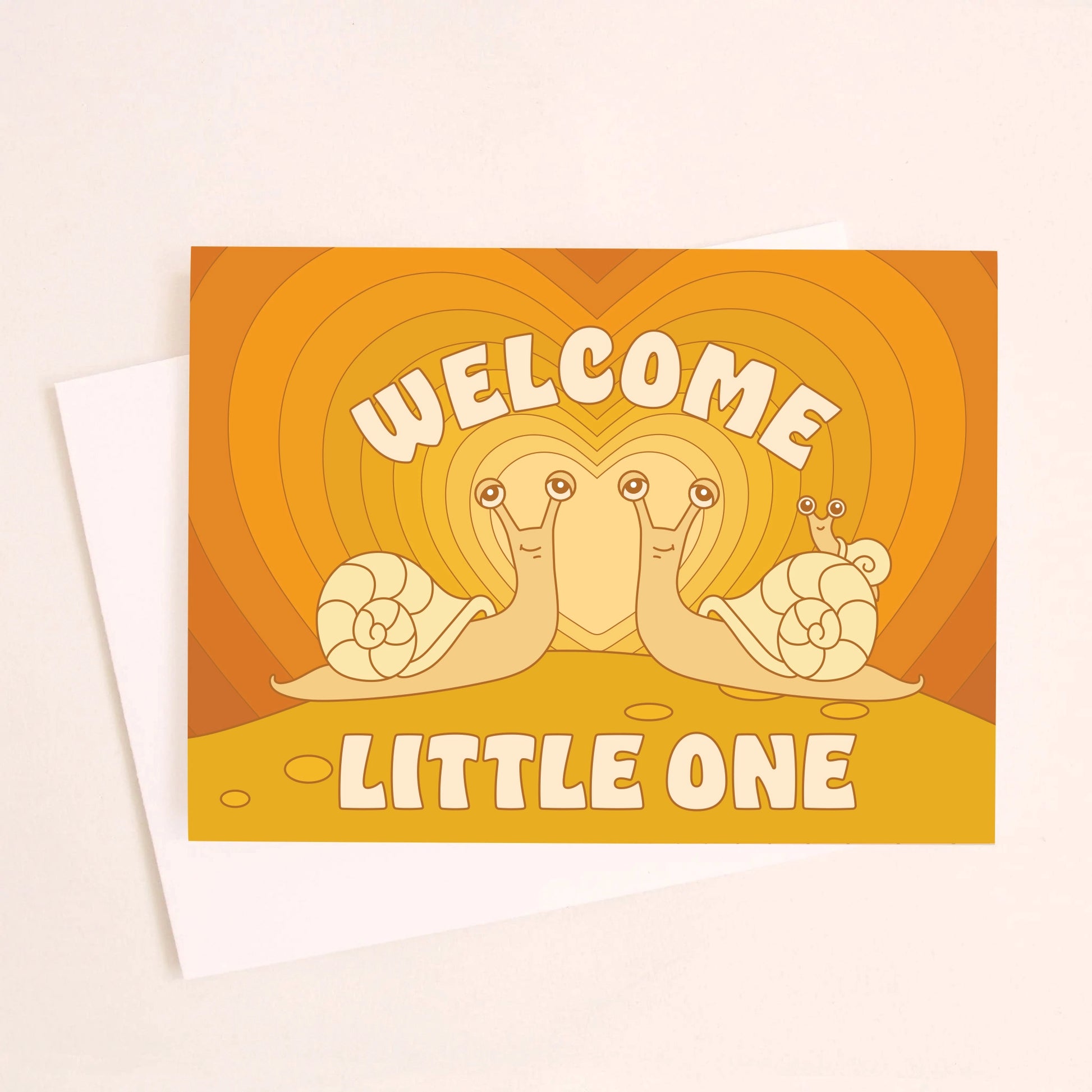 On an ivory background is an orange greeting card with an orange gradient heart background and two snails facing one another with a baby snail on the back of one along with text above and below that reads, "Welcome Little One". 