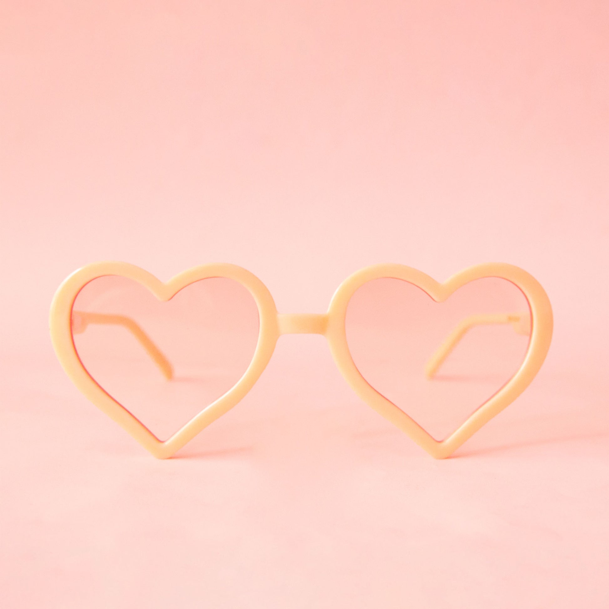 On a neutral background is a pair of apricot heart shaped glasses.
