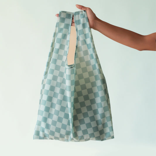 On a light blue background is an aquamarine colored nylon tote with an aqua checkered pattern all over.