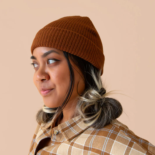 A brown knit beanie sits on a brown colored background.