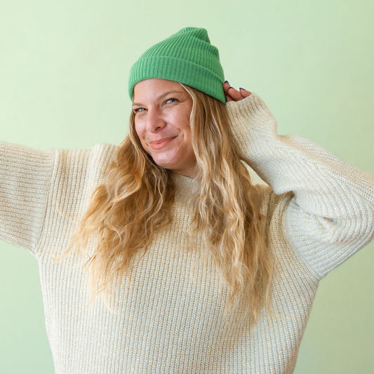 A jade colored knit beanie sits on a mint green ground.