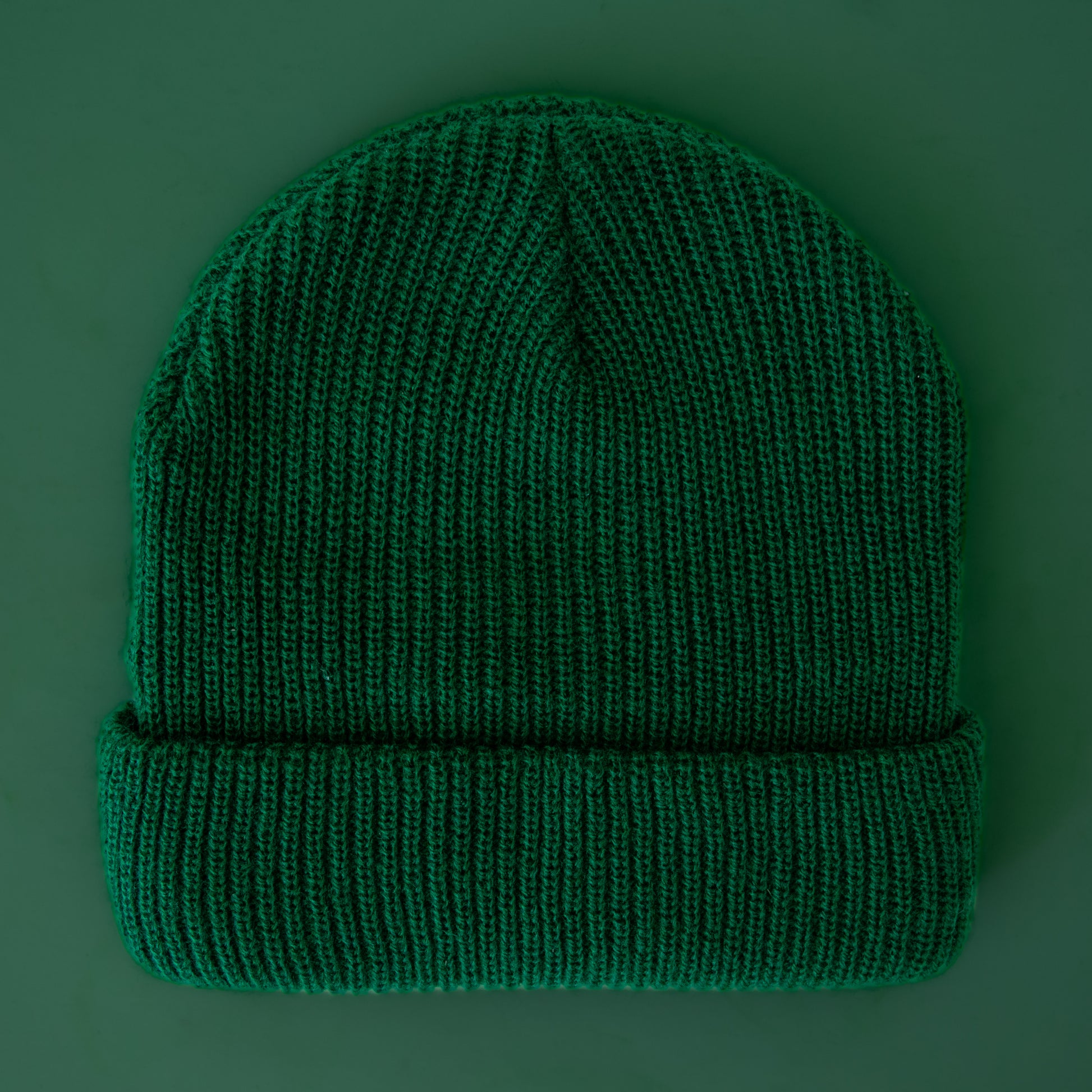 An emerald colored knit beanie sits on a green background.