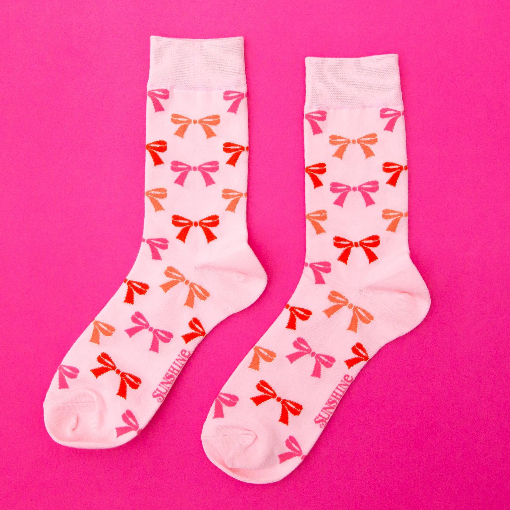 A pair of pink socks with an orange, red and pink bow pattern. 