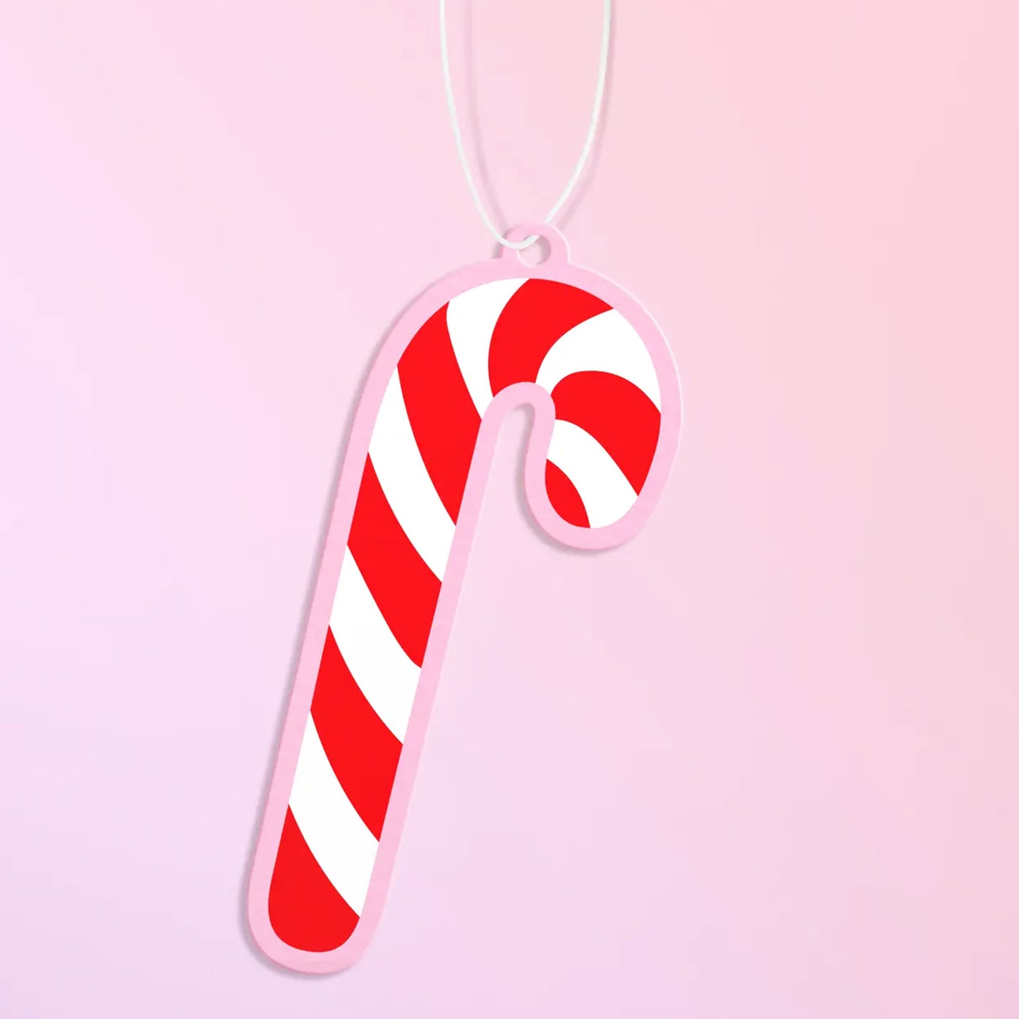 Red and white candy cane air freshener with a baby pink boarder is shows against a light pink background. 