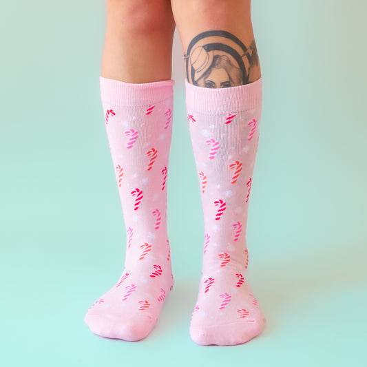 A pair of pink crew socks with a pink candy cane pattern. 