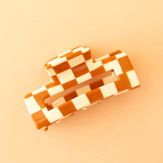 On a tan background is an ivory and orange rectangle claw clip.