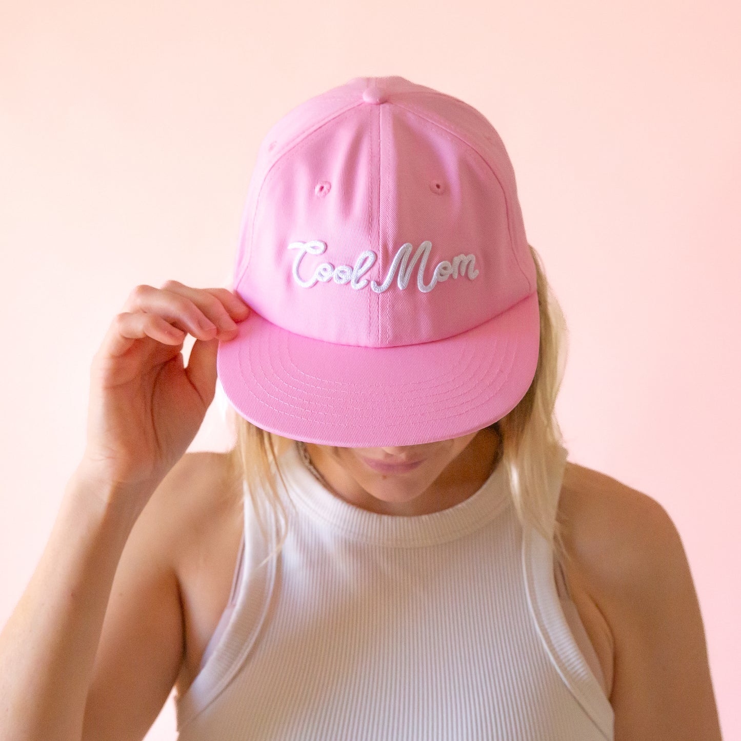 A pink flat brim hat with white embroidered text that reads, 'Cool Mom'. 